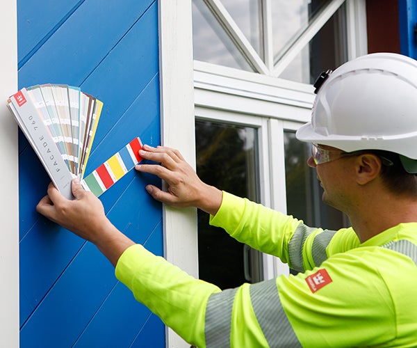Worker in PPE checking paint swatches against building