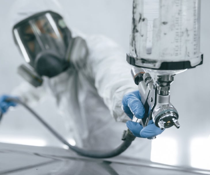 A person in a white protective suit painting a car