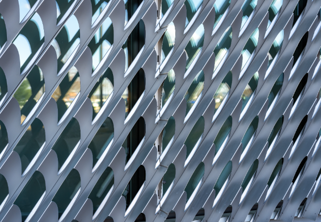 Close-up photo of silver gray angled exterior aluminum louvers over a buildings windows - glazing