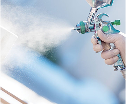 Hand holding a green metal spray gun spraying light liquid coating