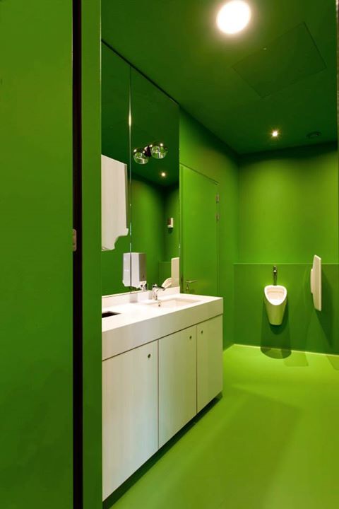 Een badkamer met groene muren en een wastafel en urinoirs