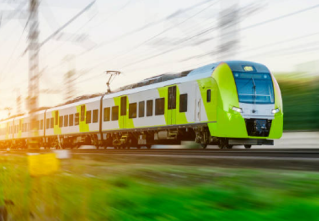 Green-and-white passenger train speeding along electrified tracks, with motion blur in the surrounding landscape.