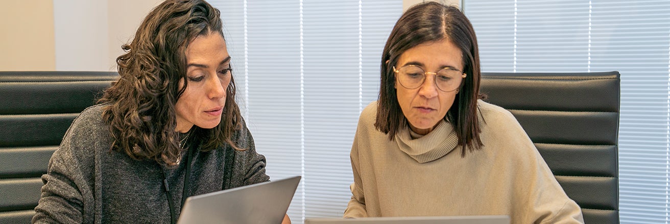 Two female colleagues discussing work using laptops