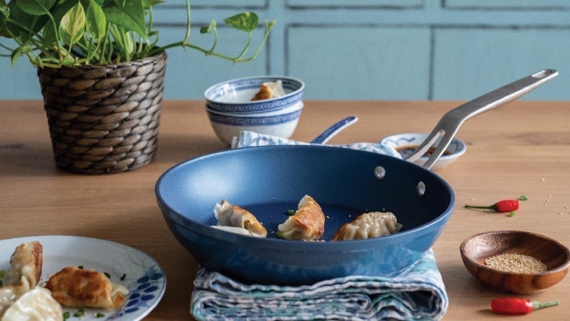 Blue kitchenware with cooked dumplings on a wooden table, accompanied by a wicker pot with a green plant, enhancing the rustic yet modern culinary ambiance
