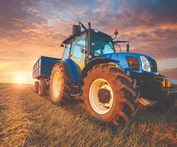 Blue tractor and trailer in a harvested field against a sunset sky
