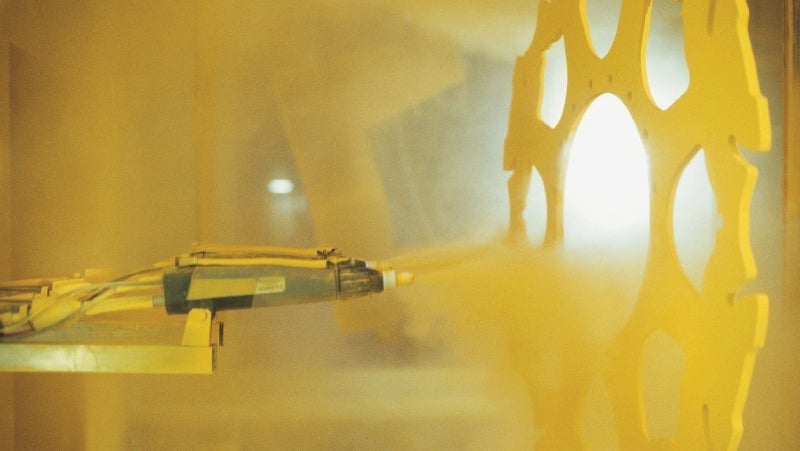 Automated industrial robot spray painting a large yellow gear in a manufacturing setting