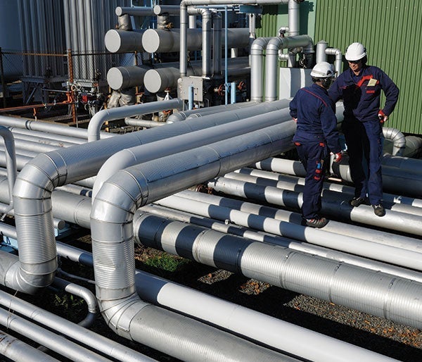 Men in overalls standing on a large pipe
