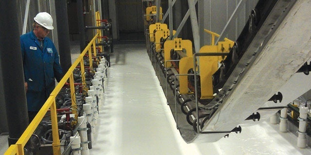 Worker in blue overalls and hard hat inspecting a row of industrial machinery inside a modern manufacturing plant