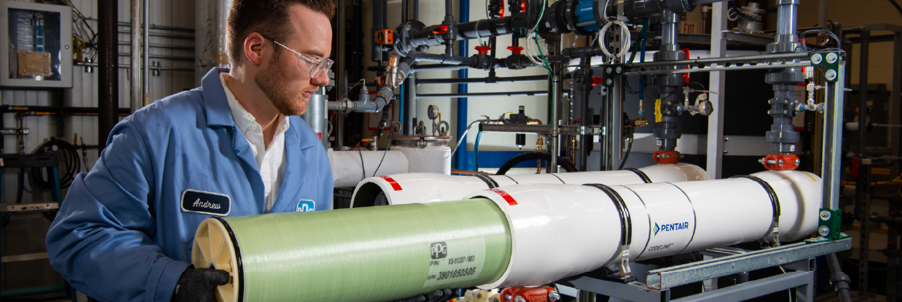A technician holds a cylindrical filtration membrane while inspecting an industrial water treatment system.