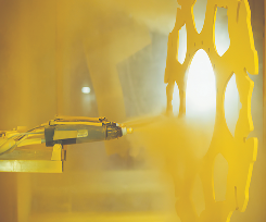 Hung metal component being sprayed with yellow powder