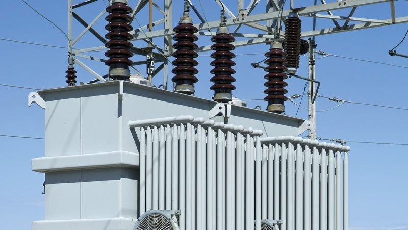 Detailed view of an industrial power transformer with high-voltage insulators and a steel tower under a clear blue sky