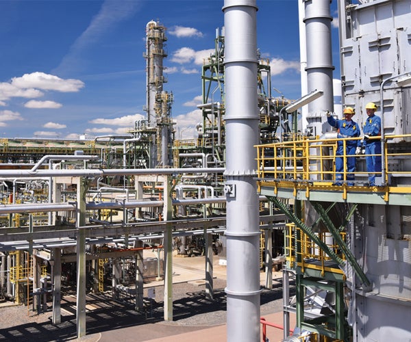 Two workers observing pipe structures at refinery