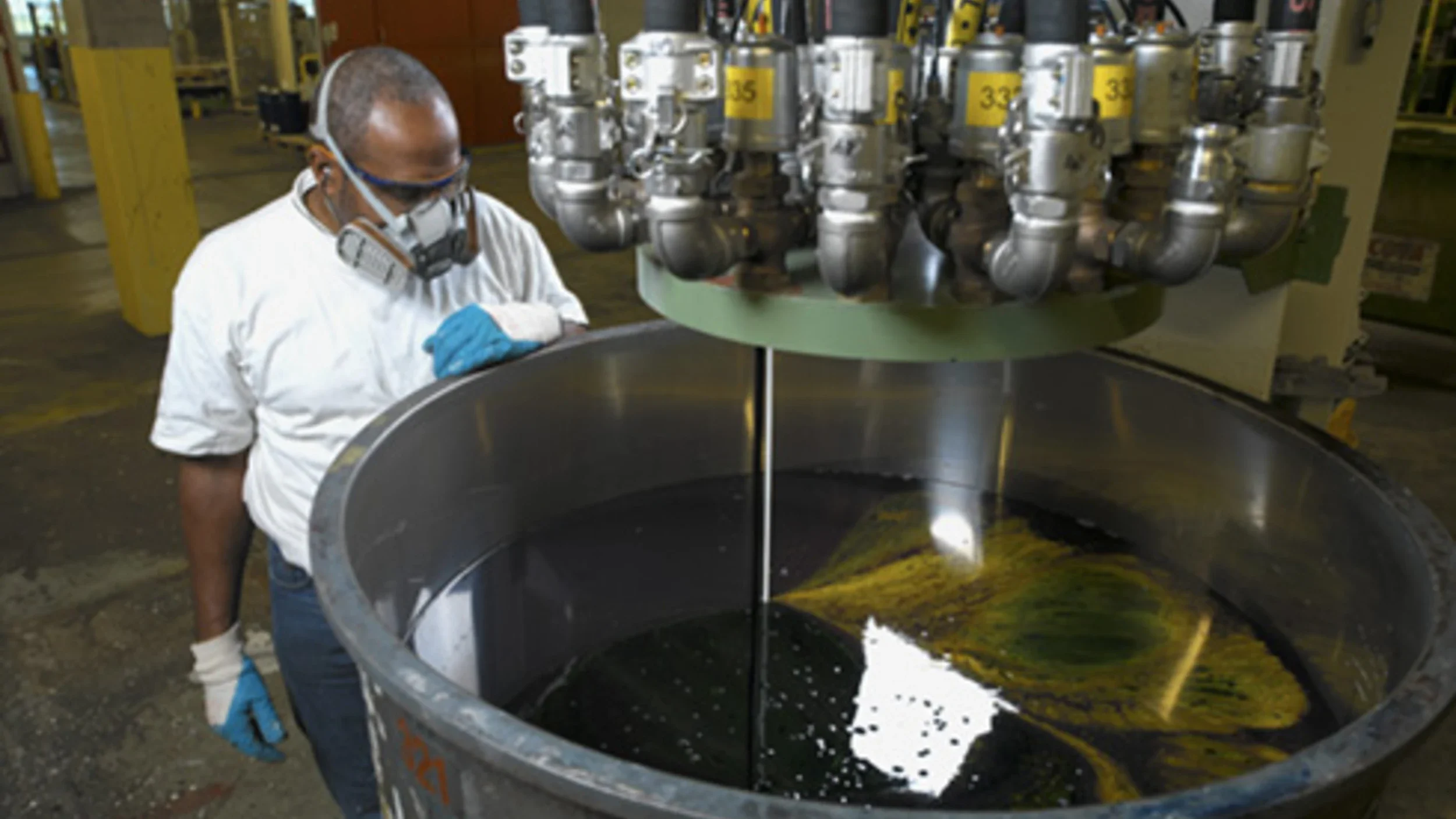 Een man met een masker en handschoenen die in een fabriek aan het werk is