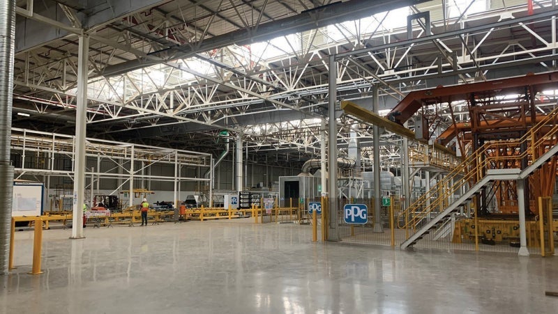 Spacious industrial factory floor with structural steelworks, overhead cranes, and scattered machinery under bright lighting