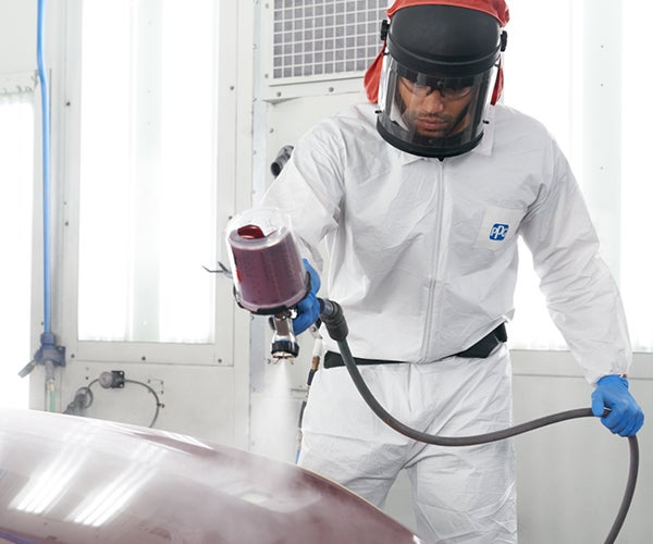 Worker using spray gun to coat vehicle in booth
