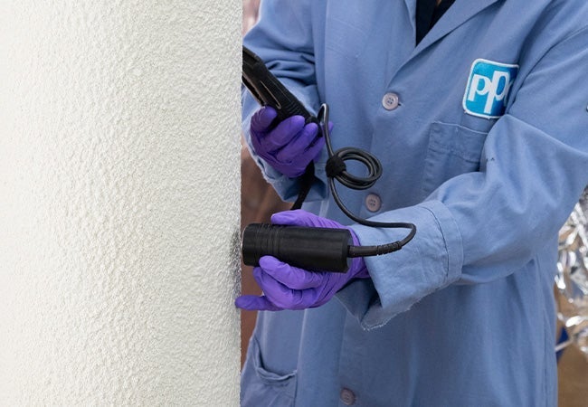 A person in a blue lab coat holding a black device