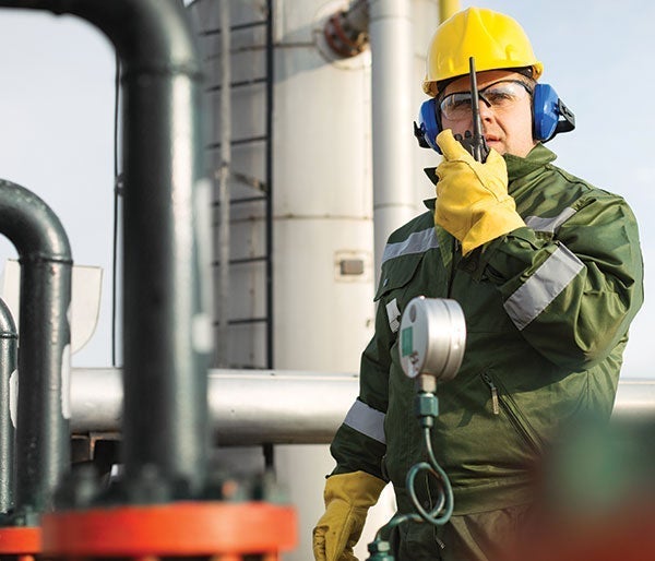 A man in a hard hat and gloves talking on a walkie talkie
