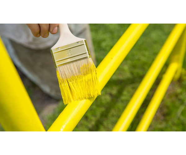 Ruka držící štětec nad žlutě natřenými kovovými trubkami