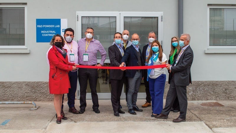 Group of professionals in business attire cutting a red ribbon at the grand opening of a new research and development lab