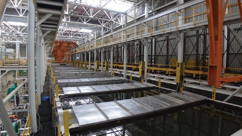 Interior view of a large industrial factory with high ceilings, overhead cranes, and rows of metal panels