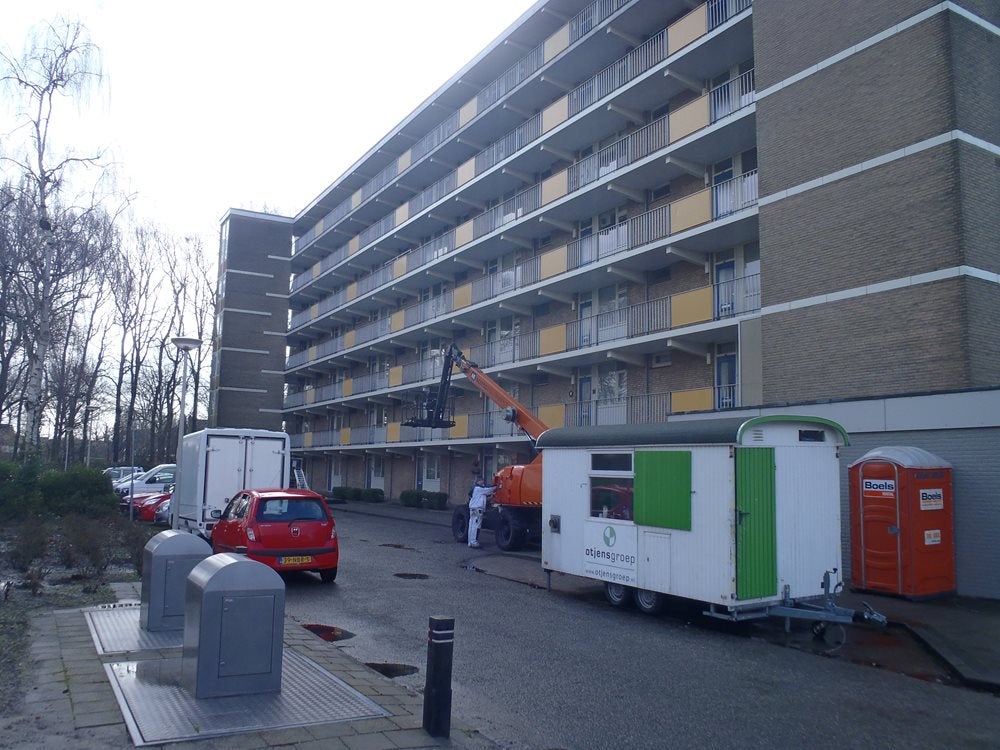 Een kraan hijst een trailer buiten een gebouw