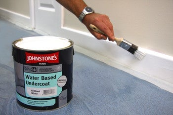 Man painting floorboard white with Johnstone's Water Based Undercoat
