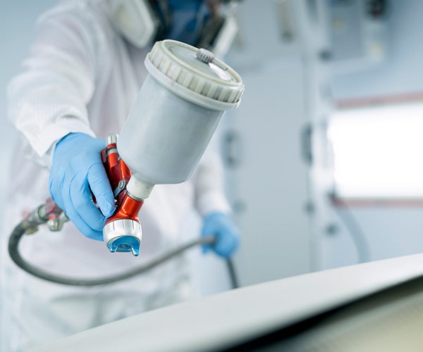 Worker in PPE using spray gun to coat vehicle