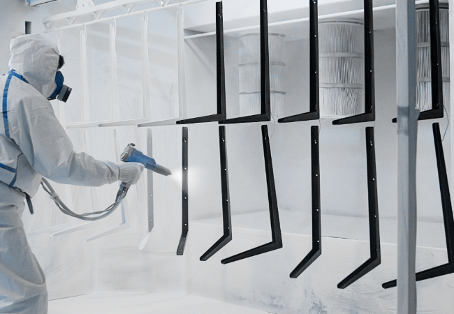 Man wearing white protective clothing spraying powder on to metal components