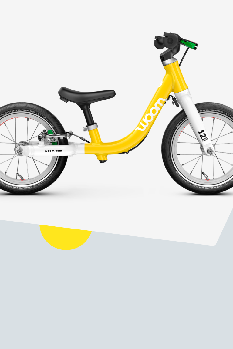 A yellow woom GO 1 balance bike with 12" wheels for children aged approximately 18 months and upwards, viewed from the side