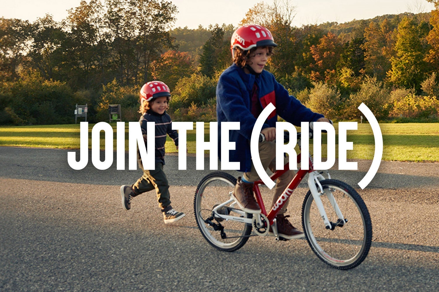 A child rides his red woom GO bike while his sibling runs behind him