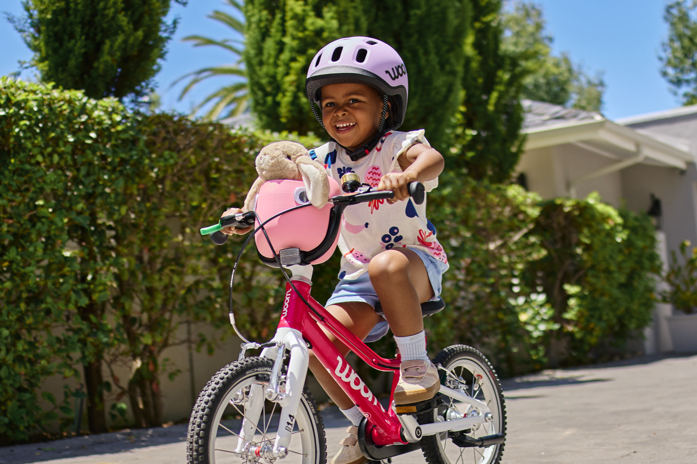Ein Mädchen fährt auf dem neuen woom 2; darauf steckt der woom Fahrradkorb in der neuen Farbe pink. Darin sitzt ein Kuscheltier.