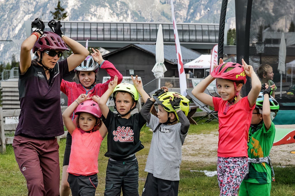 Eine Gruppe von Kindern macht eine lustige Übung mit einer Bike-Instruktorin. Alle tragen Fahrradhelme.