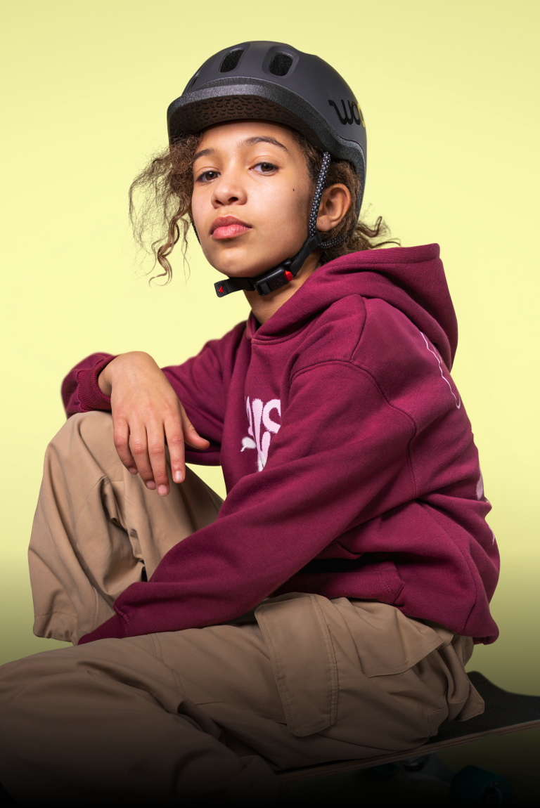 Une jeune fille portant un casque enfant READY noir de woom pose assise avec un bras posé sur sa jambe relevée.