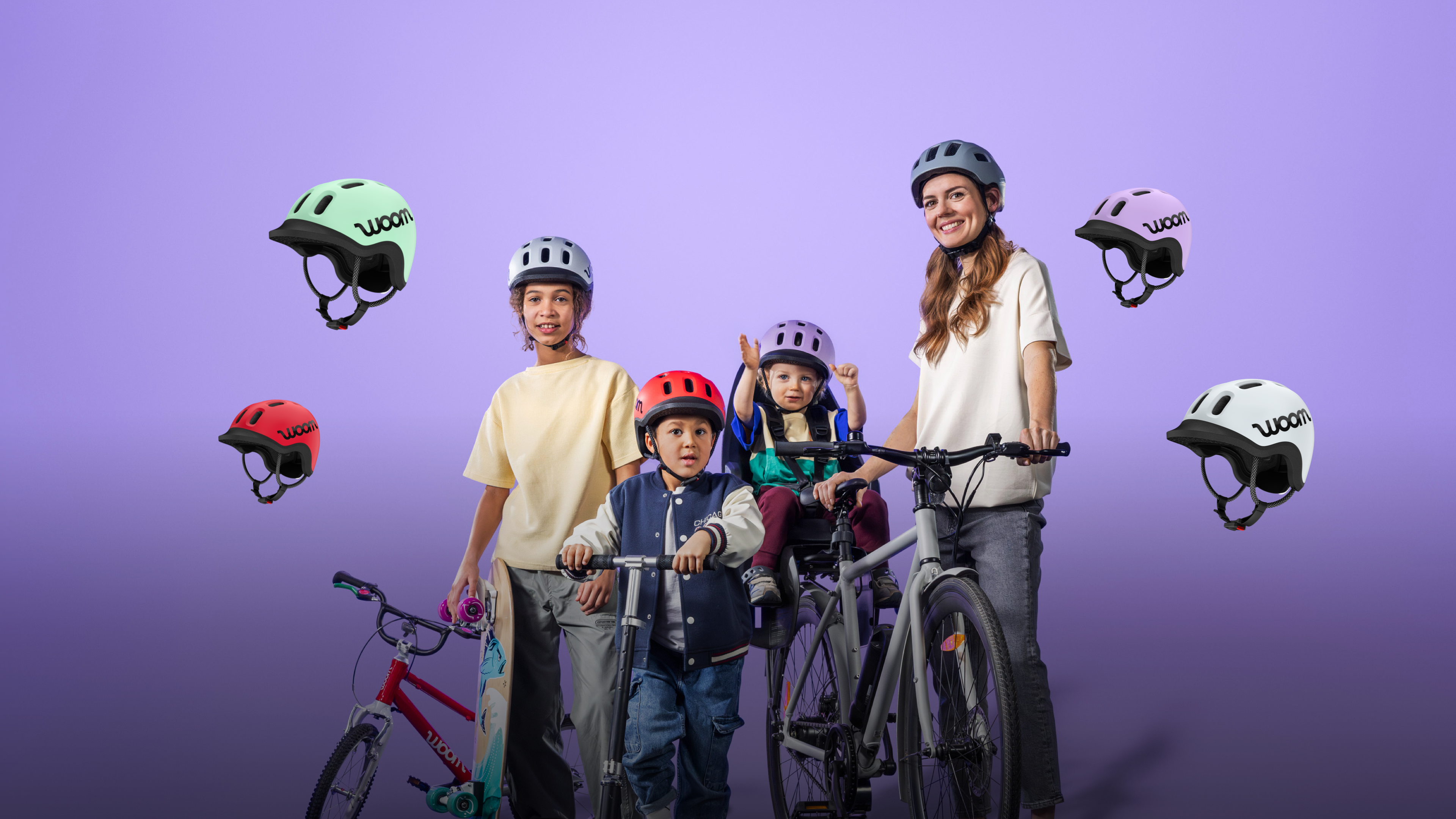 Une femme avec son enfant dans un siège vélo, 2 enfants avec skateboard et trottinette, tous portent le casque READY de woom
