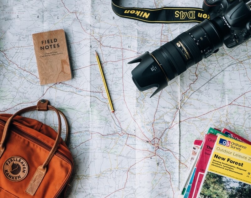 Photo by Annie Spratt on Unsplash, which shows a map laid out with a large camera, hand bag and the books on top with a pencil