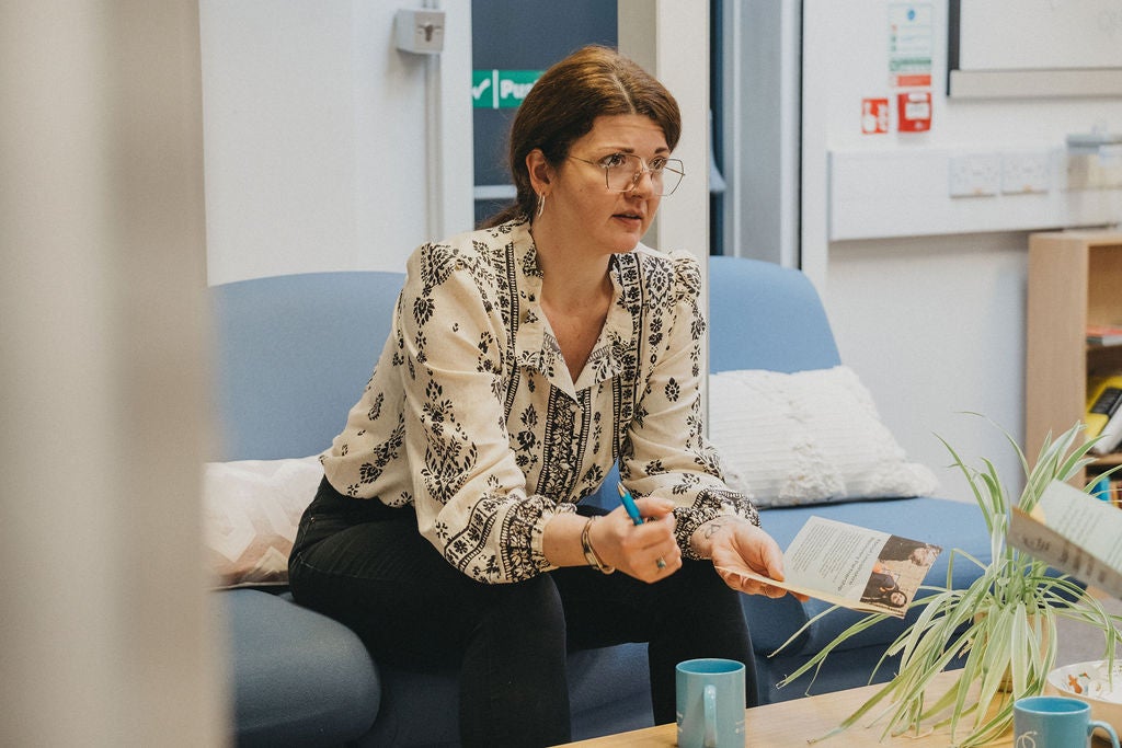 A woman sitting on a couch holding a pen and a book