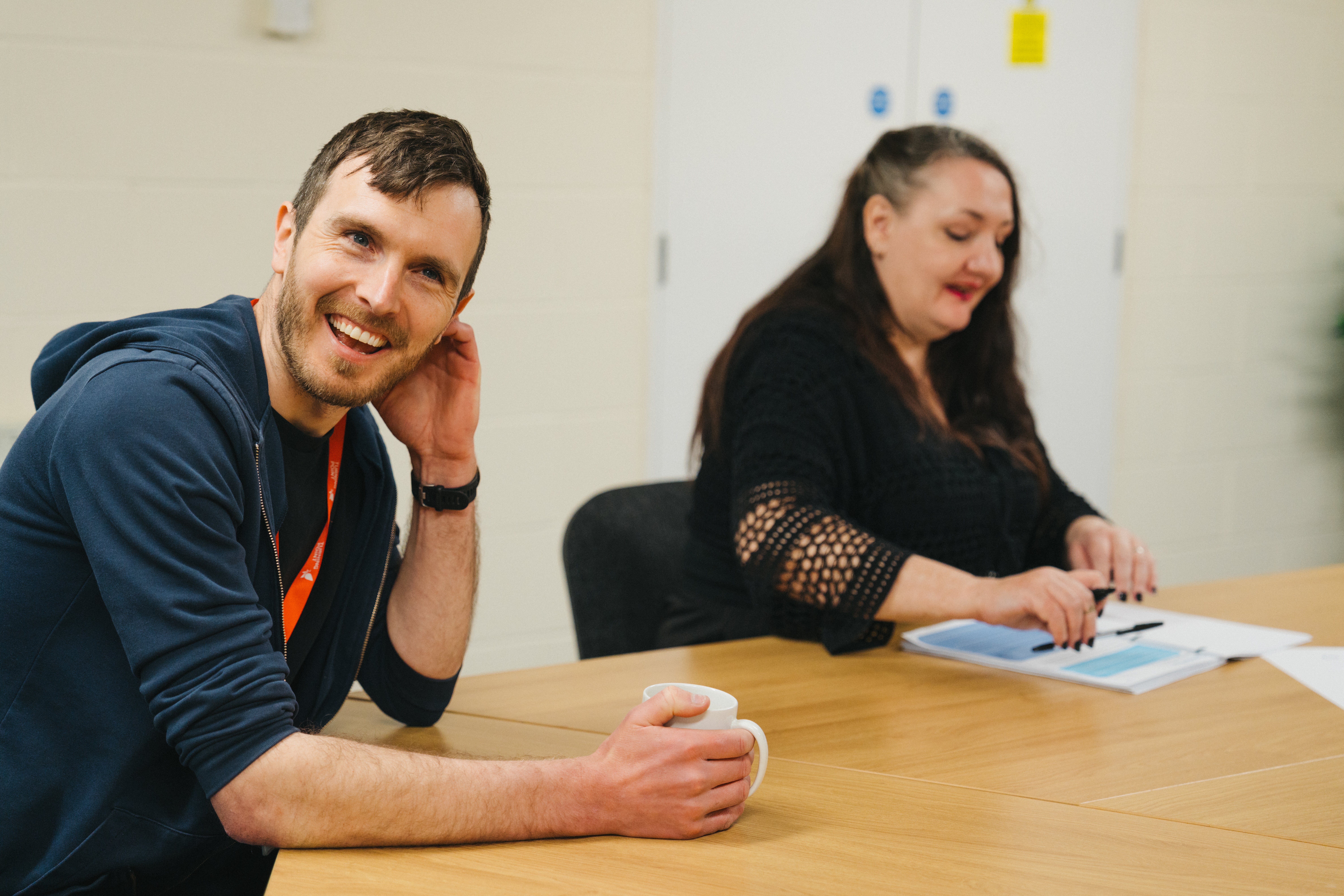 A male sitting at a table with another lady reading a booklet