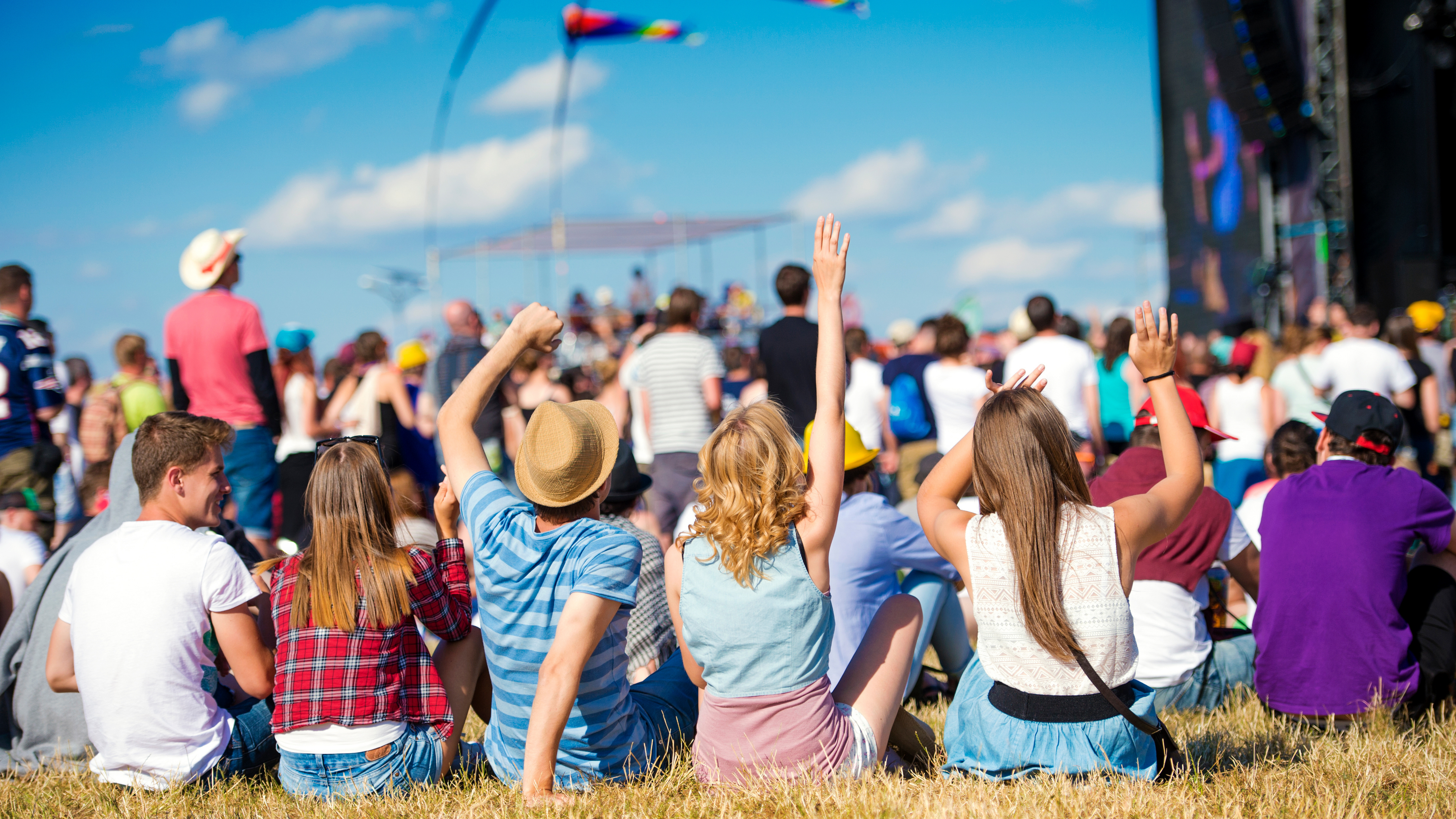 people sitting down at a festival in front of a stage in the sunshine