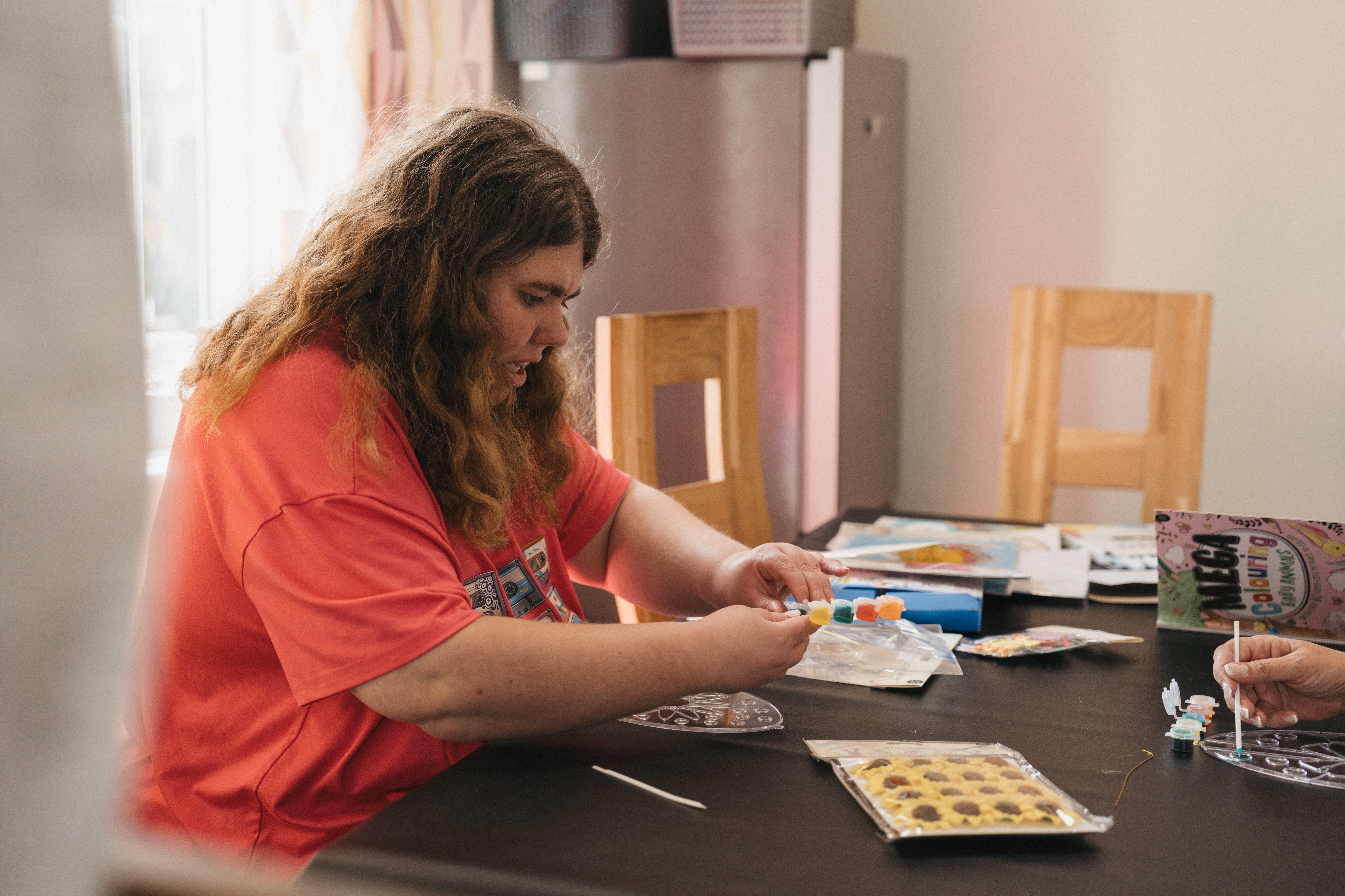 A person with long curly hair sitting at a table doing arts and crafts