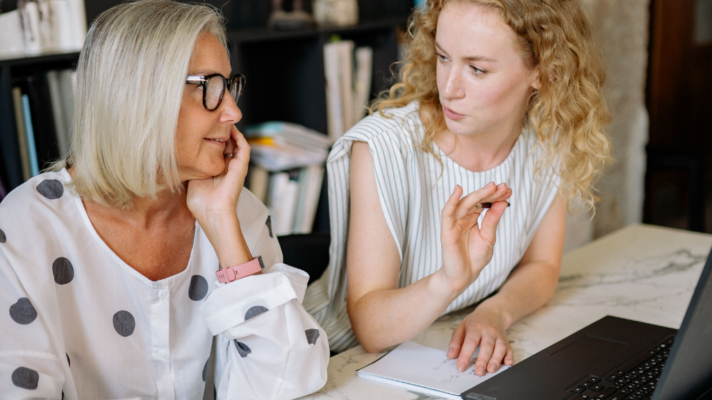 A younger woman talking to a mature woman in front of a work laptop