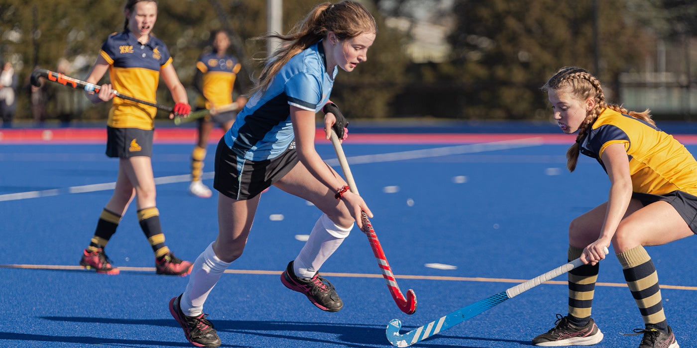 Female Hockey player in Yellow Tacking a female hockey player in blue