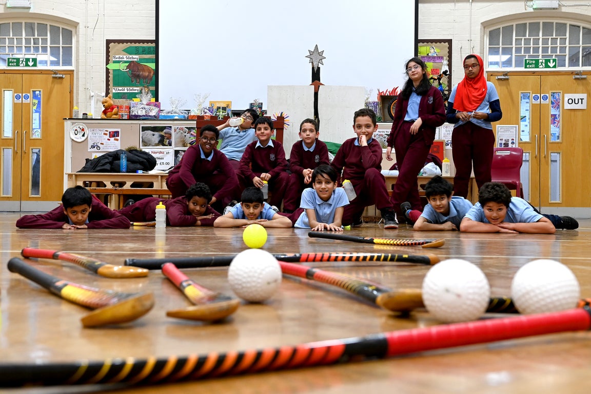 School children in a hall with hockey sticks and balls