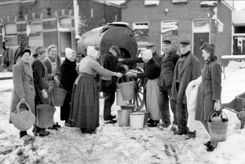 Mensen staan naast een tankwagen en vullen emmers met water.