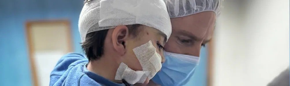 ICRC surgeon Jan ICRC surgeon Jan holds a young child with a bandaged head in a hospital setting.