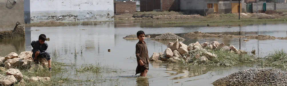 A child sits on some rocks at the side of flood water while another child stands in a river during the aftermath of the Pakistan floods 2022. 