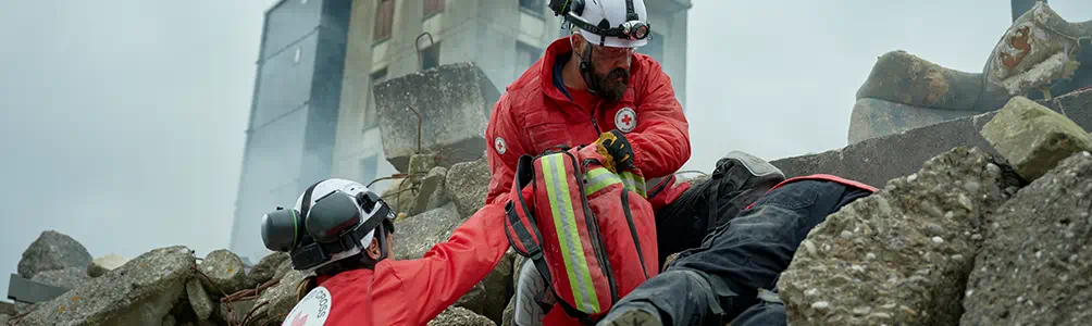 Red Cross workers search rubble to reach people caught in a disaster area.
