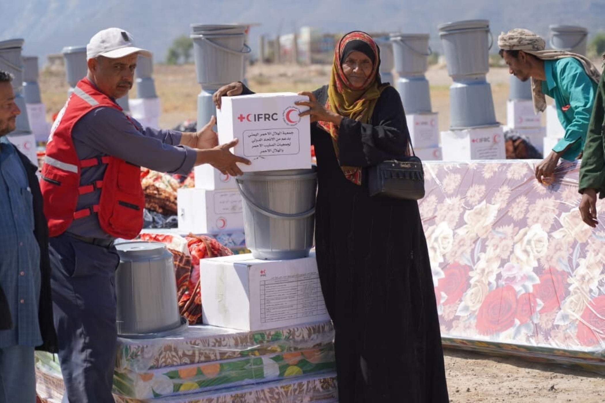 Yemen Red Crescent volunteer hands an IFRC relief box to a woman during flood response efforts.