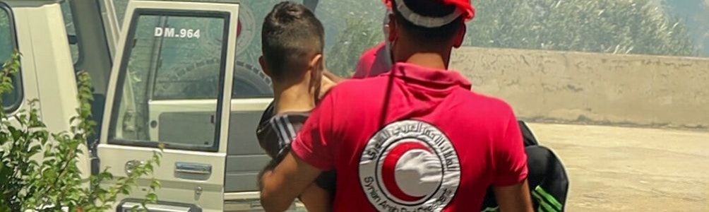 Syrian Arab Red Crescent worker carrying a young boy to safety near an ambulance.