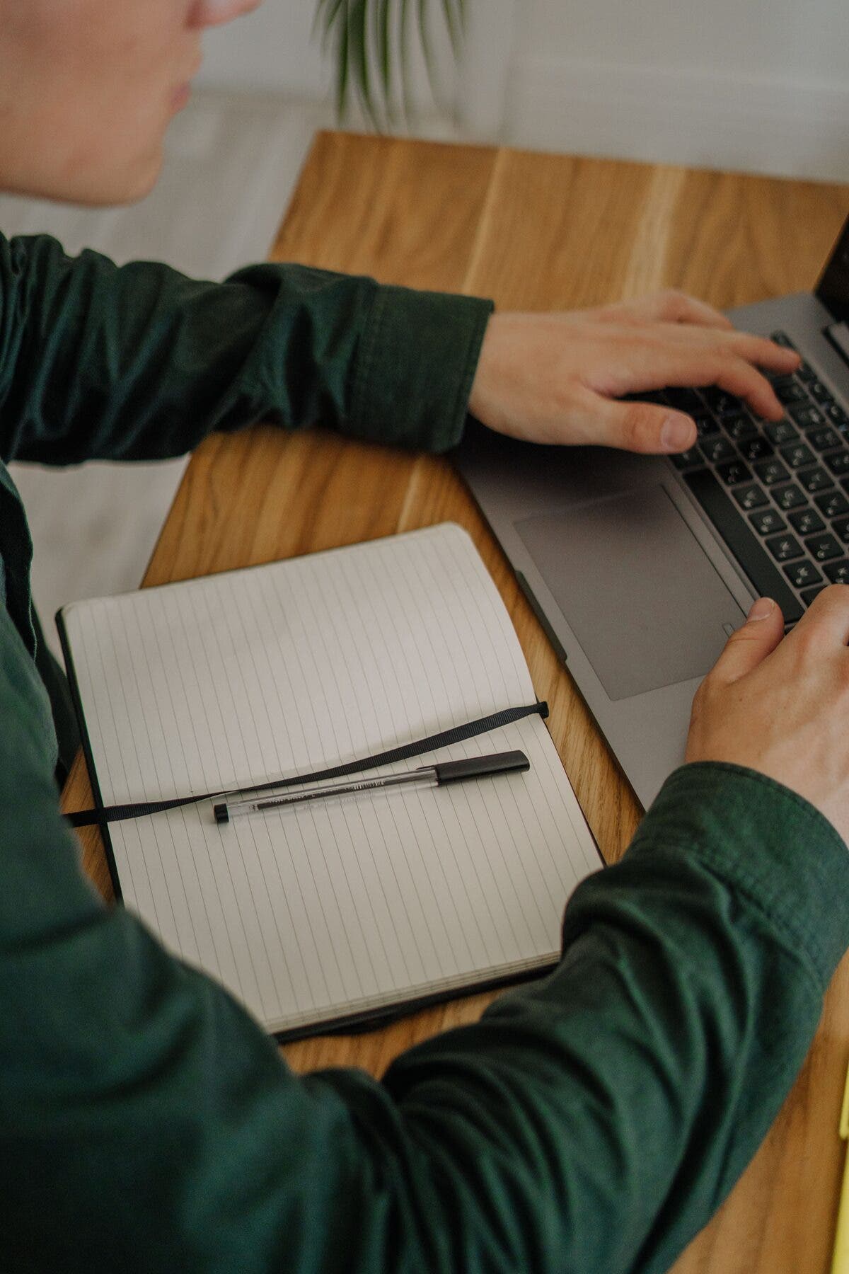 Mains sur un ordinateur portable, à côté d’un carnet