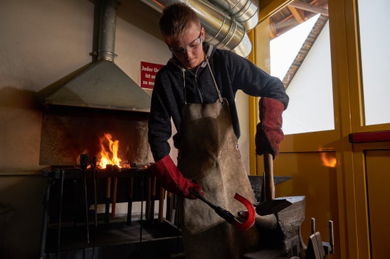 Schüler vor einer Esse formt ein Hufeisen